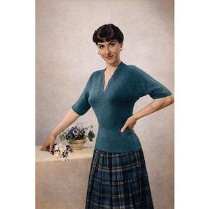 May include: A teal-colored knit top with a V-neck and short sleeves, paired with a plaid skirt. The top has a textured design along the neckline and sleeves. A small bouquet of flowers sits on a table.