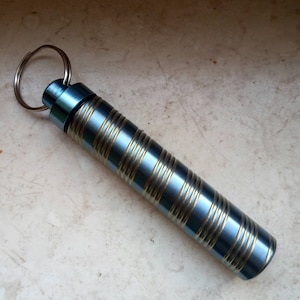 May include: A blue metal keychain with a gold striped design. The keychain has a small ring for attaching keys.