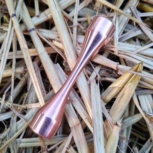 Puede incluir: Un tubo de metal de color cobre con un extremo redondeado. El tubo est&aacute; sobre un lecho de paja.
