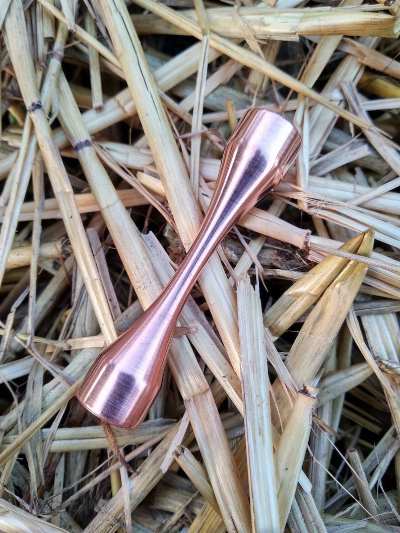 Puede incluir: Un tubo de metal de color cobre con un extremo redondeado. El tubo est&aacute; sobre un lecho de paja.