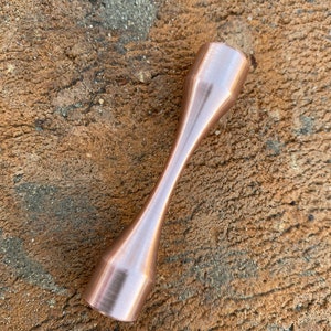 Puede incluir: Un esp&eacute;cimen de prueba de tracci&oacute;n de metal de color cobre con un acabado liso y pulido.