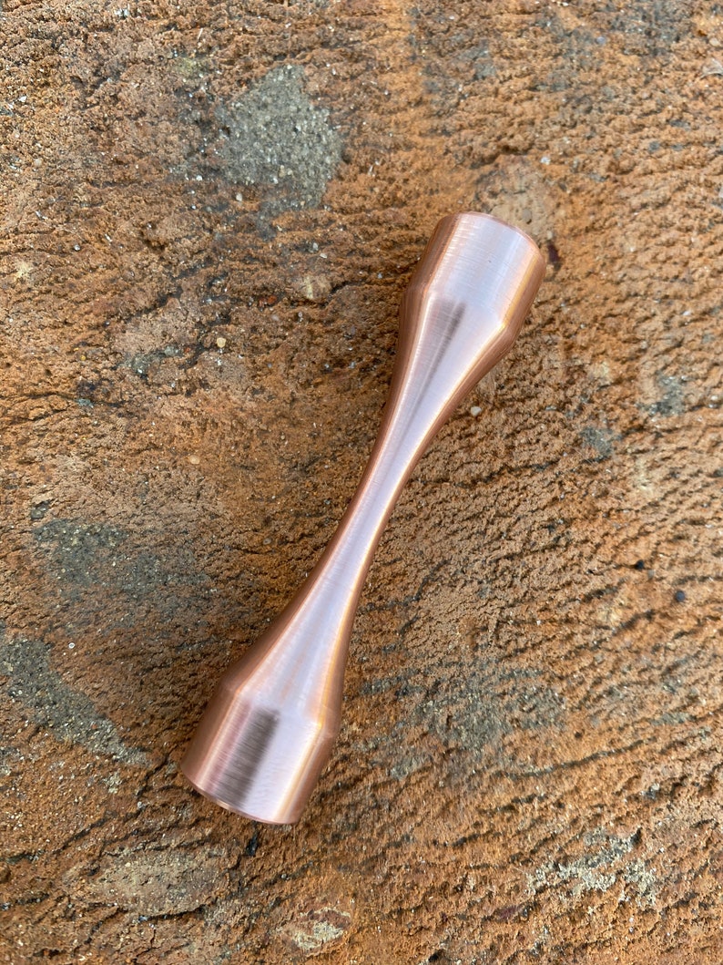 Puede incluir: Un esp&eacute;cimen de prueba de tracci&oacute;n de metal de color cobre con un acabado liso y pulido.