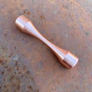 Puede incluir: Una mancuerna de metal de color cobre con un acabado liso y pulido.