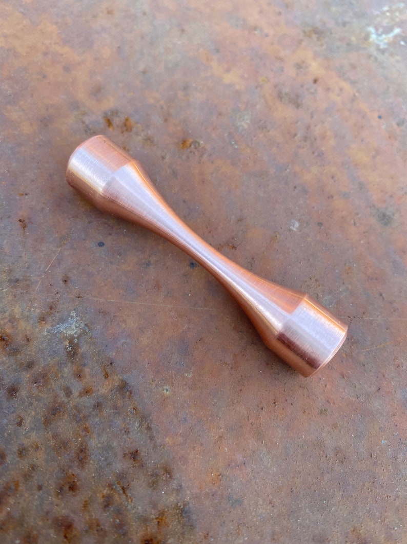 Puede incluir: Una mancuerna de metal de color cobre con un acabado liso y pulido.