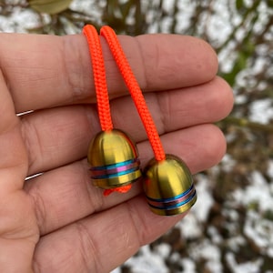 Può includere: Due giocattoli fidget in metallo color oro con una fascia arcobaleno attorno al centro, collegati da una corda arancione brillante.