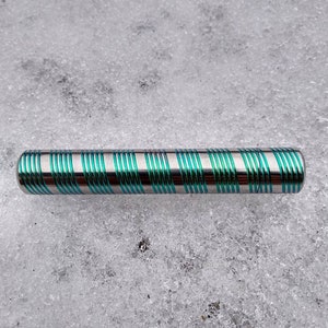Puede incluir: Un tubo de metal plateado con rayas verdes que recorren toda su longitud. El tubo está sobre una superficie blanca.