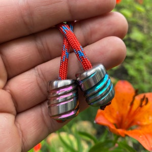 May include: Two small, iridescent metal fidget toys with a swirling pattern, attached to a red and blue braided cord.
