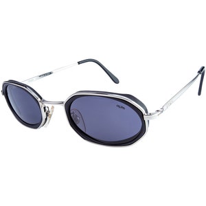 May include: Silver-framed sunglasses with black octagonal lenses and a black trim. The sunglasses have a silver metal frame and black plastic arms. The brand name "Old Skool" is printed on the right lens.