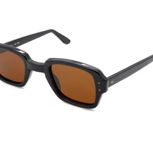 Puede incluir: Gafas de sol rectangulares negras con lentes marrones. Las gafas tienen un estilo cl&aacute;sico y retro.