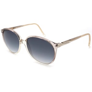 May include: Clear-framed sunglasses with gradient gray lenses. The oval-shaped frames have a subtle, translucent quality, and the temples are a light beige color. The sunglasses have a classic, vintage aesthetic.