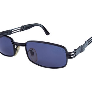 May include: Black sunglasses with a metal frame and blue lenses. The sunglasses have a unique design with multiple metal bars on the arms. The text "LO228" is printed on the right lens.