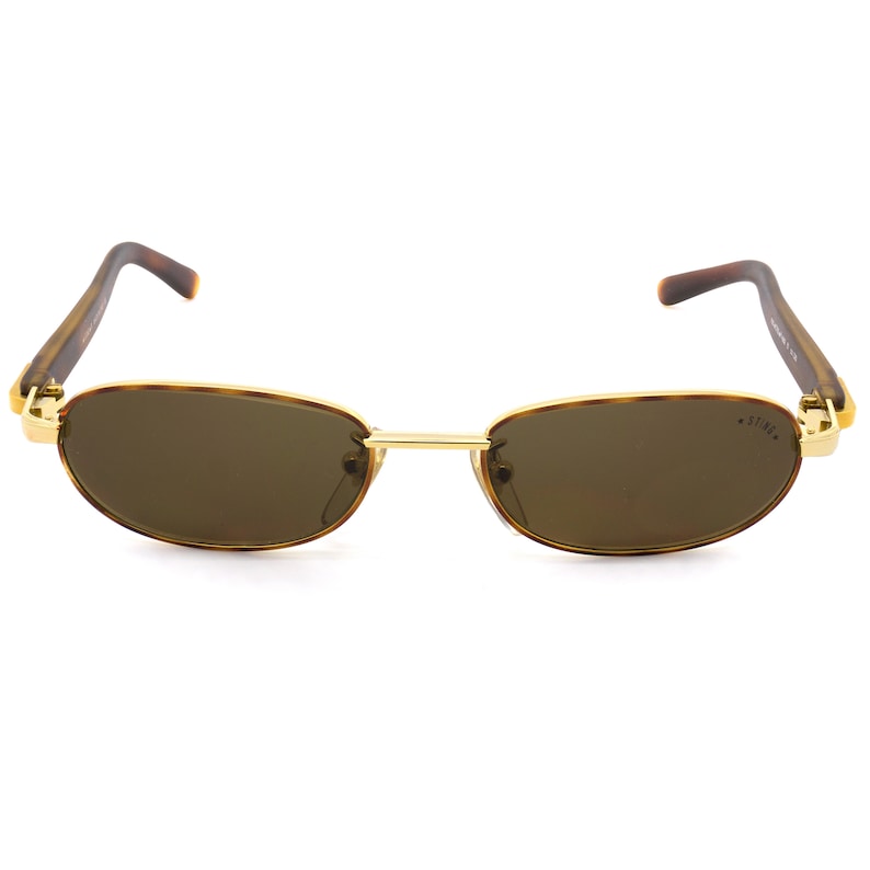 Puede incluir: Un par de gafas de sol ovaladas de carey marr&oacute;n con monturas de metal dorado y lentes marrones. Las gafas de sol tienen la palabra "STING" escrita en la lente derecha.