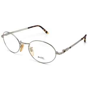 May include: Silver-toned oval-shaped eyeglasses with a thin metal frame and clear lenses. The brand name "String." is printed on the right lens.