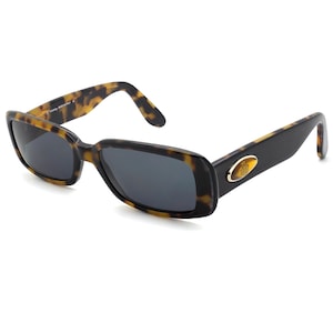 May include: Rectangular sunglasses with a tortoiseshell pattern on the upper frame and temples, and black frames. The lenses are dark gray. A gold-colored emblem is on the temple. The sunglasses are set against a white background.
