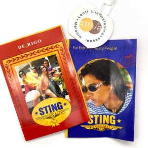 Puede incluir: Dos tarjetas promocionales rojas y azules para gafas de sol Sting. La tarjeta roja presenta a un grupo de personas con gafas de sol y el texto "DE RIGO" y "STING OCCHIALI". La tarjeta azul presenta a un hombre con gafas de sol y el texto "STING OCCHIALI".