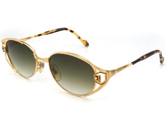 May include: Gold-tone oval sunglasses with a tortoiseshell temple and a decorative metal frame. The sunglasses have a green tint.