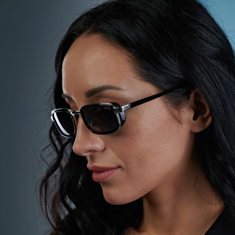 May include: A woman wearing black sunglasses with a silver frame and the word "Gucci" printed on the frame. The sunglasses have a dark lens.