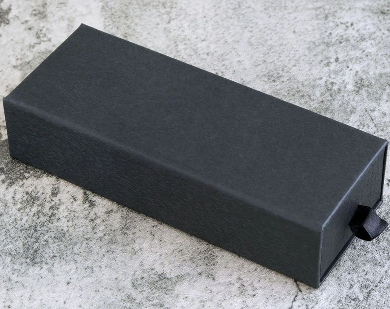 May include: A black rectangular box with a textured surface and a black ribbon pull tab.