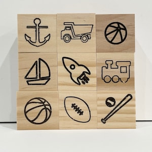 May include: Nine wooden blocks with black line drawings of various objects, including an anchor, a truck, a basketball, a sailboat, a rocket, a train, a football, a baseball and bat, and a basketball.