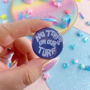 Pode incluir: Um botão azul com o texto "NO TERFS ON OUR TURF" em letras brancas.