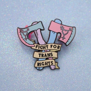 May include: A pink and blue enamel pin with two crossed axes and the text "Fight for Trans Rights".