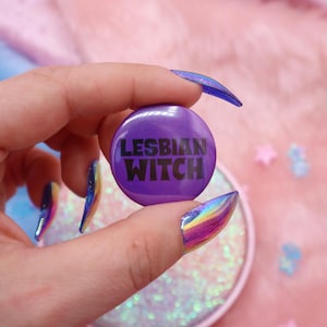 Puede incluir: Un botón morado con el texto "LESBIAN WITCH" en letras negras.