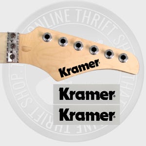 May include: Three black and white "Kramer" guitar headstock decals. The decals are on a white background and are ready to be applied to a guitar.