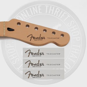 May include: Four brown Fender Telecaster guitar headstock decals with the text "Fender" and "Telecaster" in black lettering. The decals are on a white background.