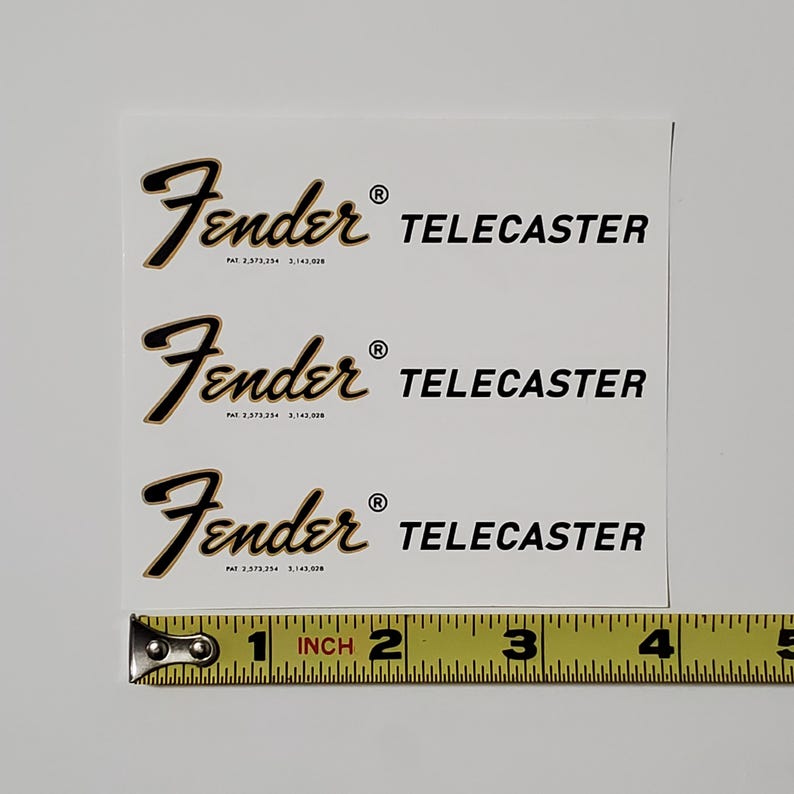May include: Three black and gold Fender Telecaster guitar headstock decals on a white background. The decals are approximately 2.5 cm in size.