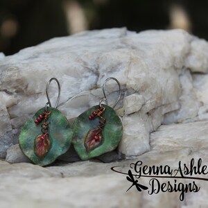 May include: A pair of green and copper earrings with a leaf design and red beads. The earrings are hanging from silver hooks.