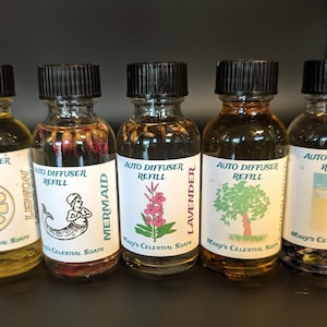 May include: Five small glass bottles with black lids and labels. Each bottle contains a clear liquid and has a different image and scent. The scents are Lemon, Mermaid, Lavender, Tree, and Coastal.