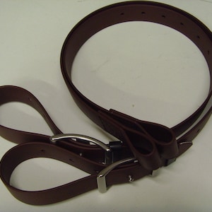 Könnte beinhalten: Ein brauner Ledergürtel mit zwei Schlaufen und einer silbernen Schnalle. Der Gürtel ist in der Mitte gefaltet und die Schlaufen sind an der Schnalle befestigt.
