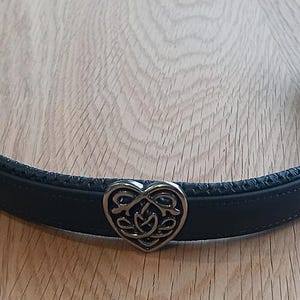 May include: Black leather dog collar with a silver heart-shaped charm featuring a Celtic knot design.
