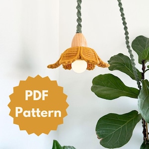 以下が含まれることがあります： 花の形をしたクロシェのランプシェードのPDFパターン。ランプシェードは黄色で、木製のベースが付いています。パターンはダウンロードできます。