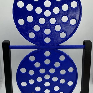 May include: A blue and black decorative object with two perforated circular discs. The discs are connected by a horizontal bar and supported by a black rectangular frame. The discs have multiple white circular holes.