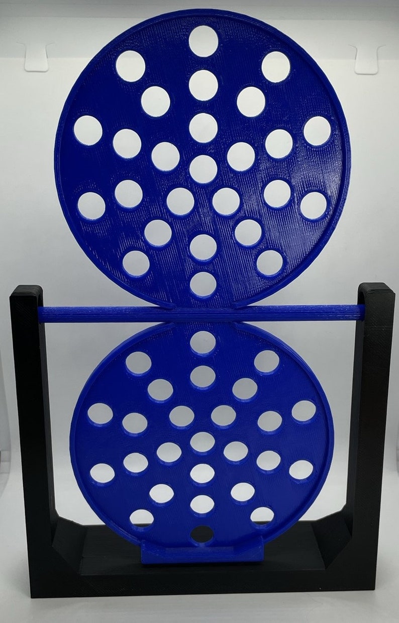 May include: A blue and black decorative object with two perforated circular discs. The discs are connected by a horizontal bar and supported by a black rectangular frame. The discs have multiple white circular holes.
