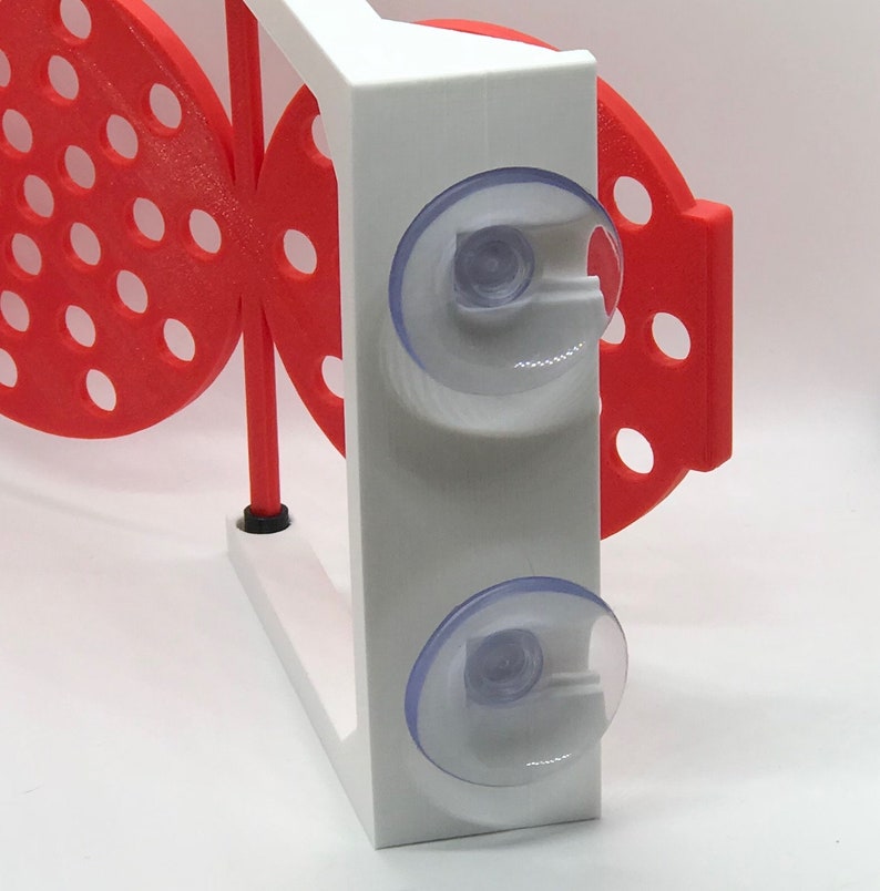May include: A white and red 3D-printed butterfly-shaped object with suction cups. The butterfly has a series of circular cutouts. The white section has two clear suction cups. The object is designed to be mounted on a smooth surface.