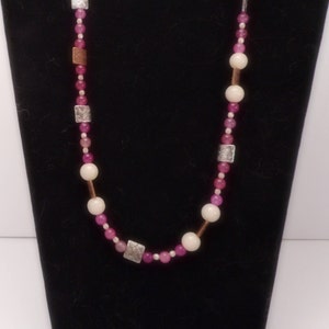 Pode incluir: Um colar de contas rosa e branco com detalhes prateados e de cobre. O colar &eacute; feito com contas redondas e quadradas.
