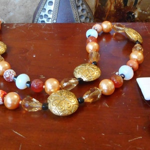 May include: A two-strand necklace with gold and brown beads, and a matching pair of earrings with red and gold beads.