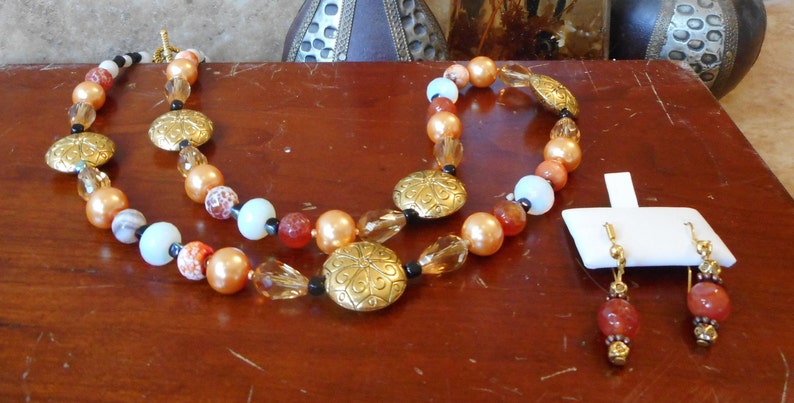 May include: A two-strand necklace with gold and brown beads, and a matching pair of earrings with red and gold beads.