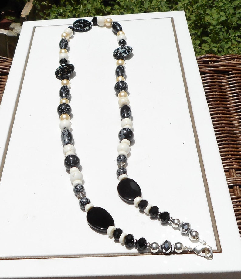 May include: A black, white, and gold beaded necklace with a black onyx pendant and a silver clasp.