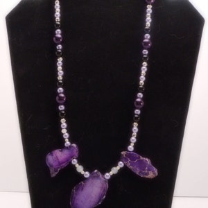 May include: A purple agate stone necklace with black, silver, and lavender beads. The necklace features three large purple agate stones.