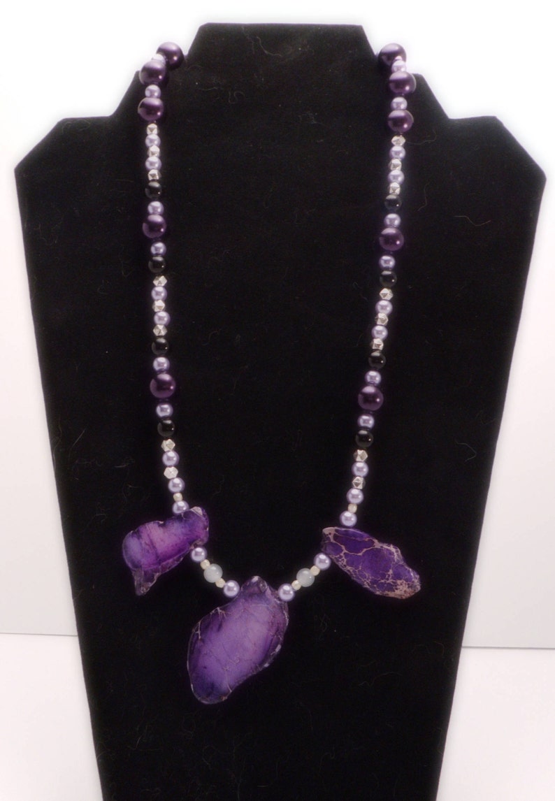 May include: A purple agate stone necklace with black, silver, and lavender beads. The necklace features three large purple agate stones.