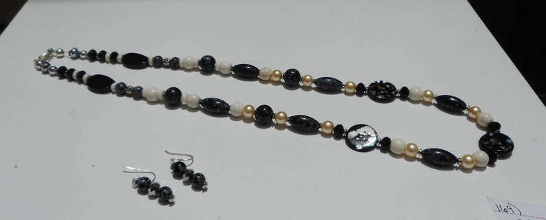 May include: A black, white, and gold beaded necklace with a large, round, black and white button pendant. Matching earrings are also included.