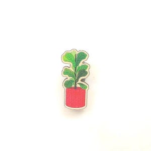 May include: A wooden pin featuring a green potted plant with a red pot. The plant has a light green stem and dark green leaves.