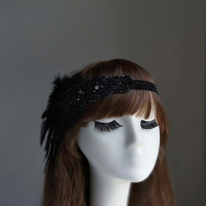 May include: A black beaded headband with a feather accent. The headband is adorned with small black beads and a single rhinestone.