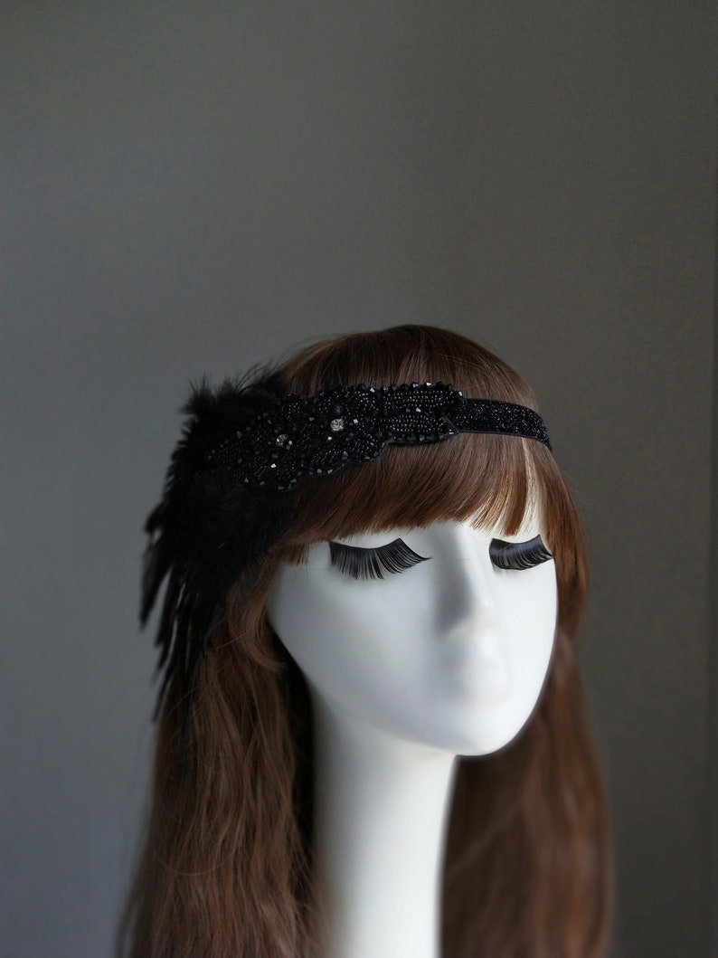May include: A black beaded headband with a feather accent. The headband is adorned with small black beads and a single rhinestone.