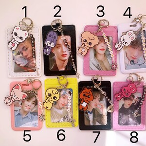 May include: Eight colorful ID card holders with keychains featuring cartoon animal charms. Each holder has a different color and design, with a clear plastic window to display an ID card. The keychains have different colored beads and charms, including a bunny, a cat, a bear, and a bird.