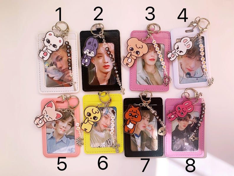 May include: Eight colorful ID card holders with keychains featuring cartoon animal charms. Each holder has a different color and design, with a clear plastic window to display an ID card. The keychains have different colored beads and charms, including a bunny, a cat, a bear, and a bird.
