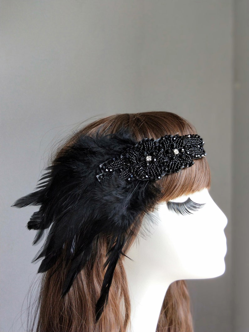May include: A black headband with a beaded design and a feather accent. The headband is worn on a mannequin with brown hair.